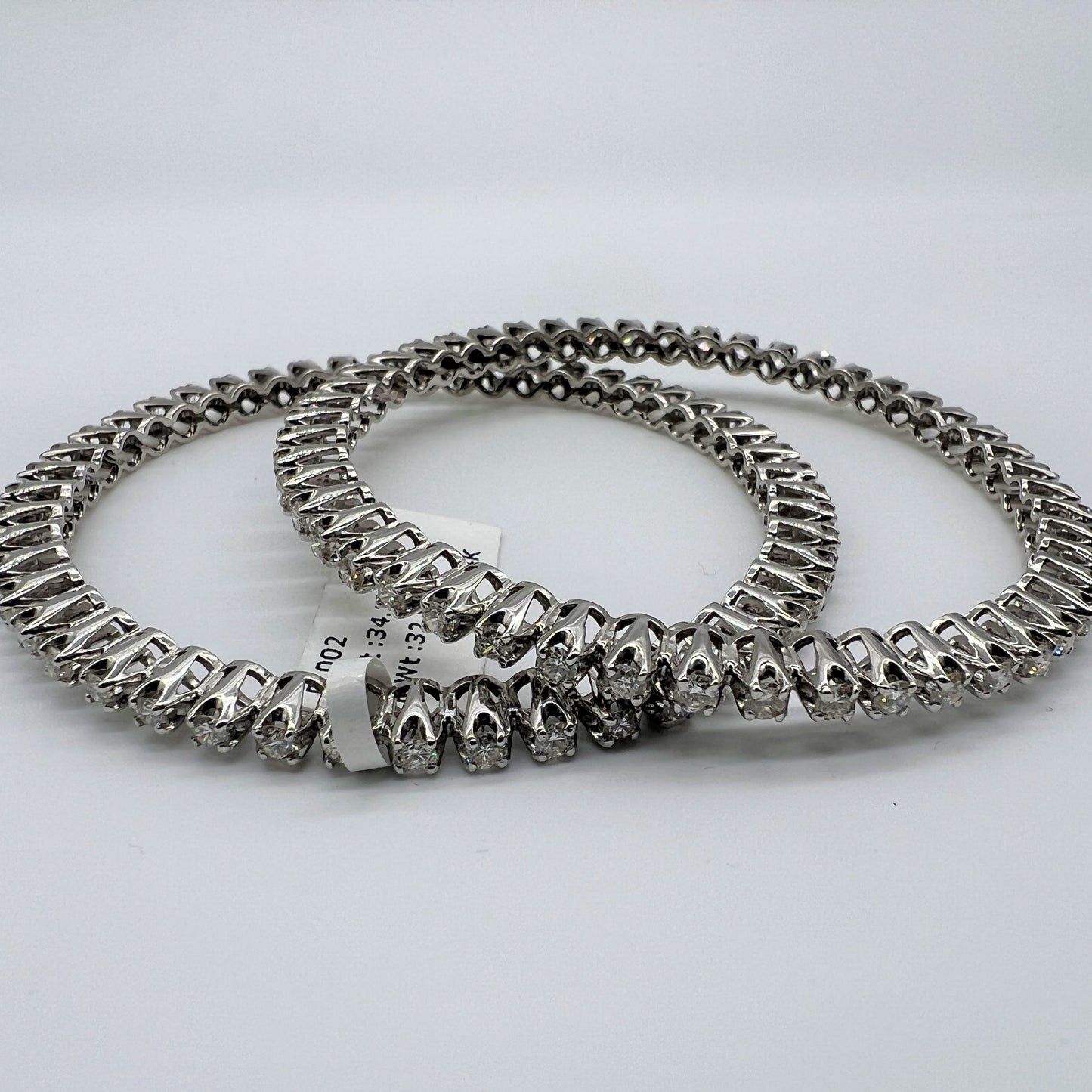 Two white gold and lab grown diamond bangles stacked on a light gray background
