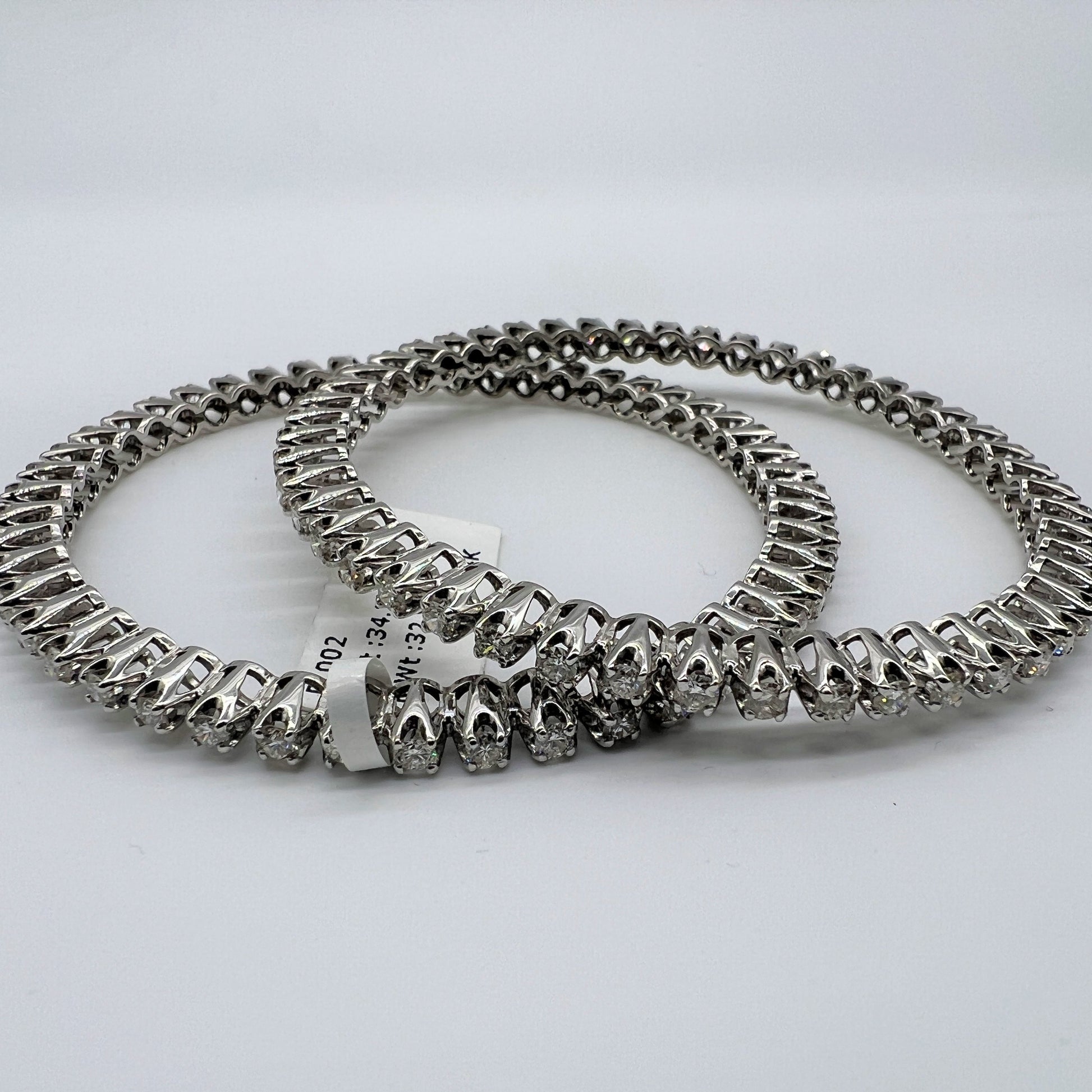 Two white gold and lab grown diamond bangles stacked on a light gray background