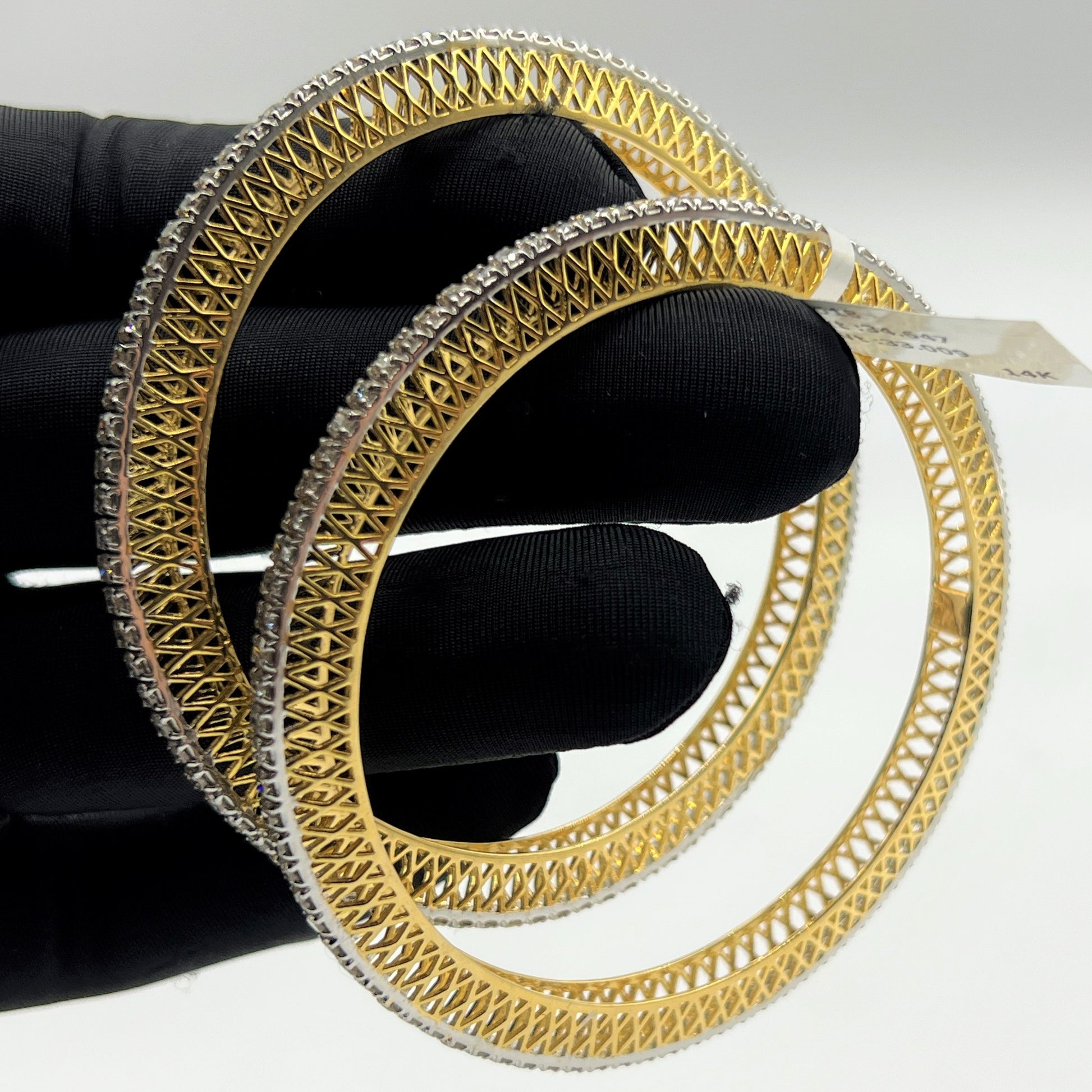 Gold and lab grown diamond bangles held by a black-gloved hand on a white background