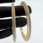 Gold bangles with lab grown diamonds on a black stand against a white background