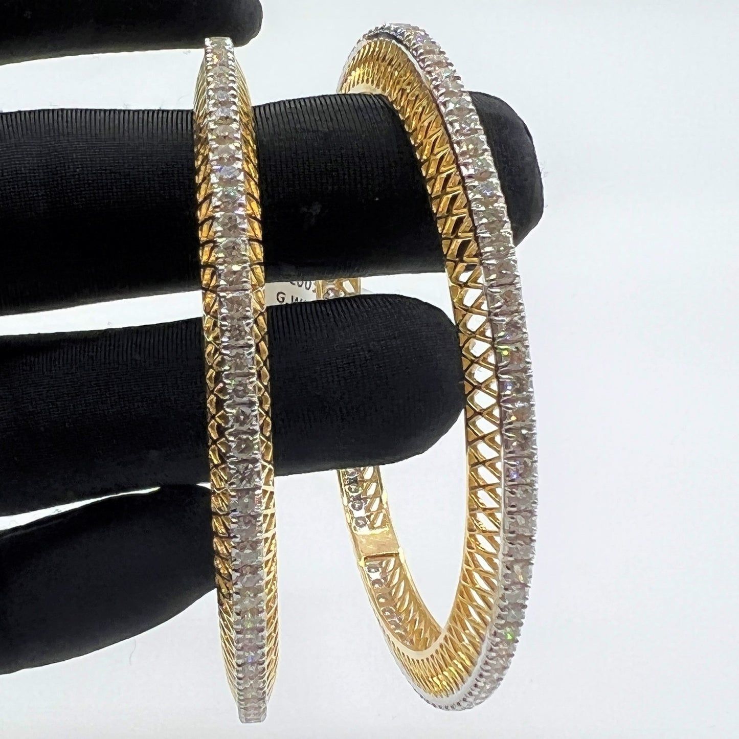 Gold bangles with lab grown diamonds on a black stand against a white background