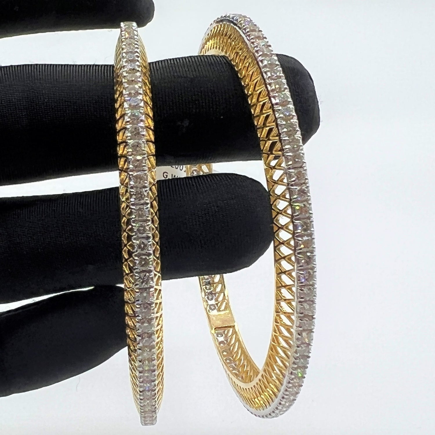 Gold bangles with lab grown diamonds on a black stand against a white background