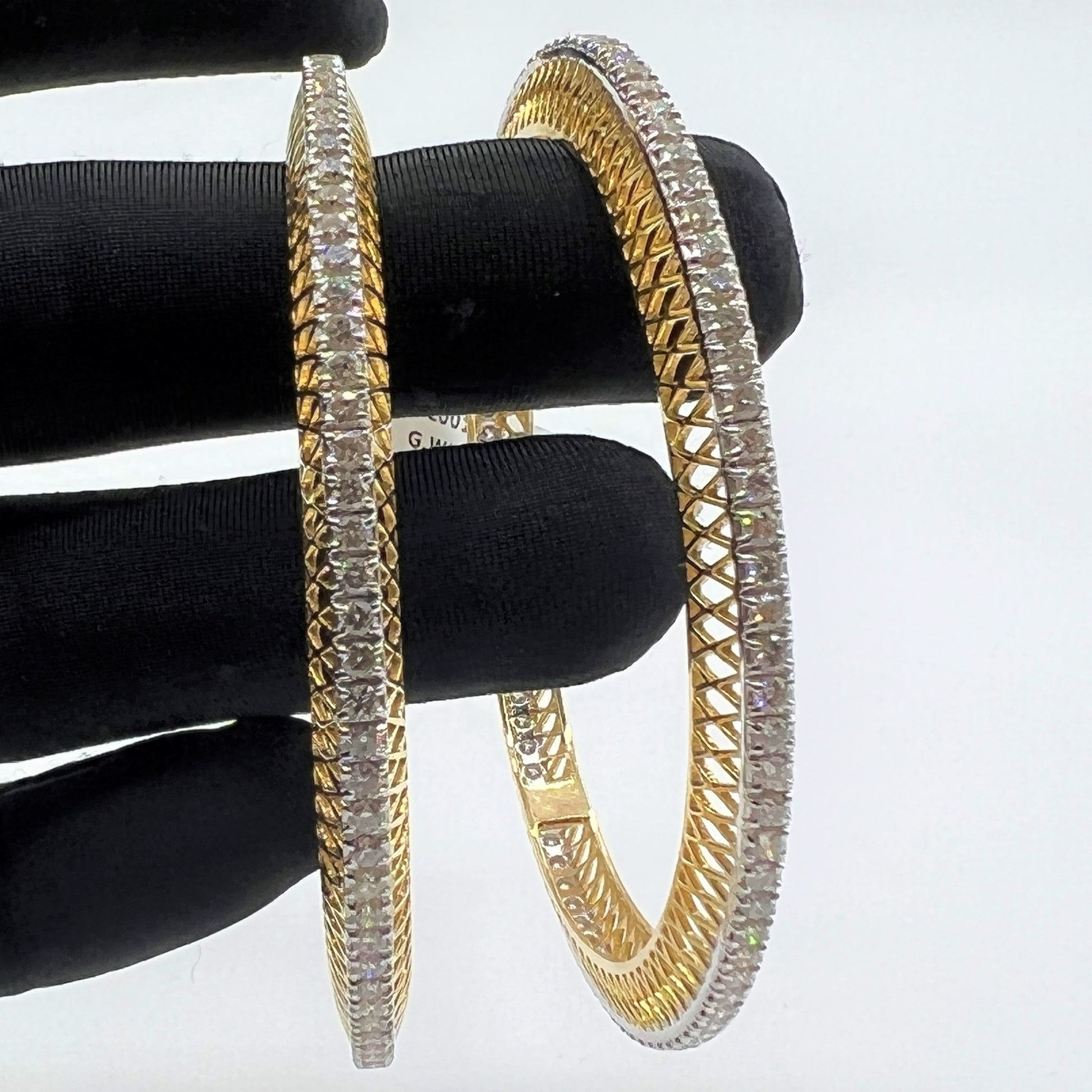 Gold bangles with lab grown diamonds on a black stand against a white background