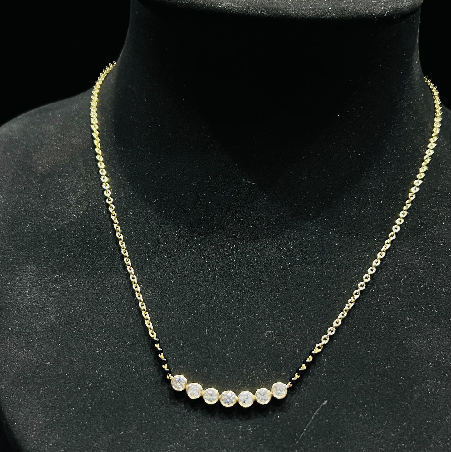 Gold and lab grown diamond mangalsutra with small round beads on a black mannequin bust