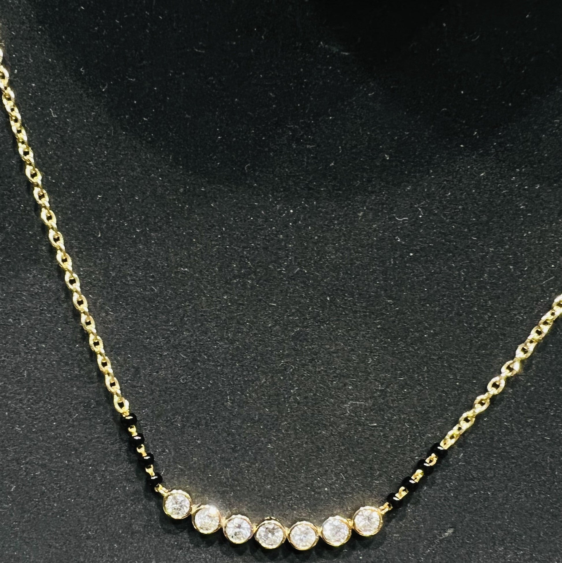 Gold mangalsutra with small round lab grown diamonds on a black background