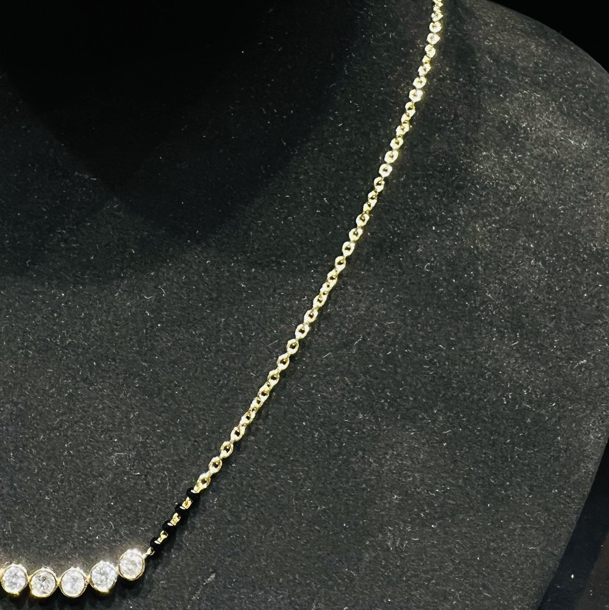 Gold mangalsutra with small round lab grown diamonds on a black mannequin.