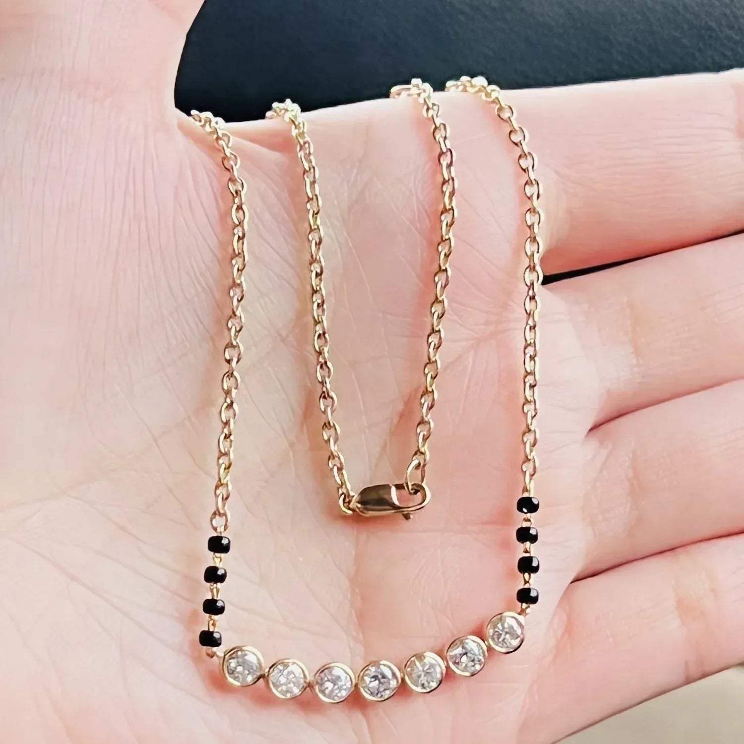Gold chain mangalsutra with black beads and clear lab grown diamonds held in a hand.