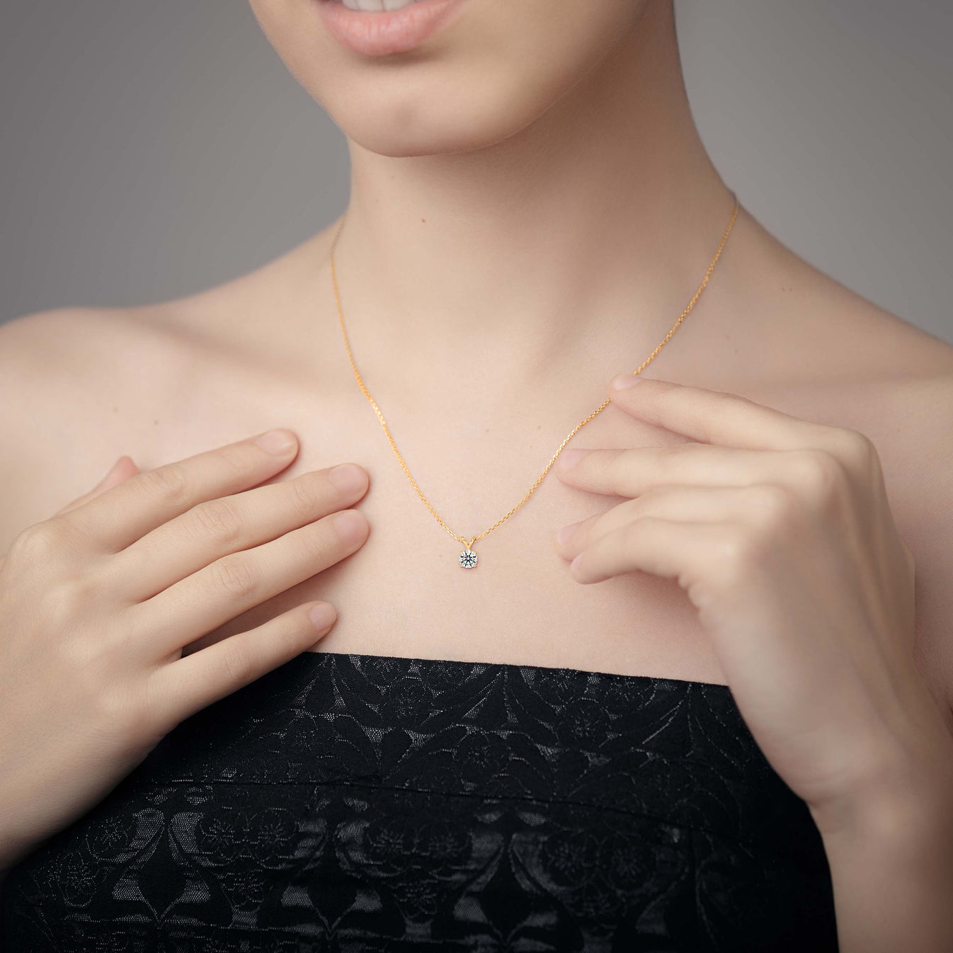 Person wearing a gold solitaire lab grown diamond pendant necklace, hands adjusting it.