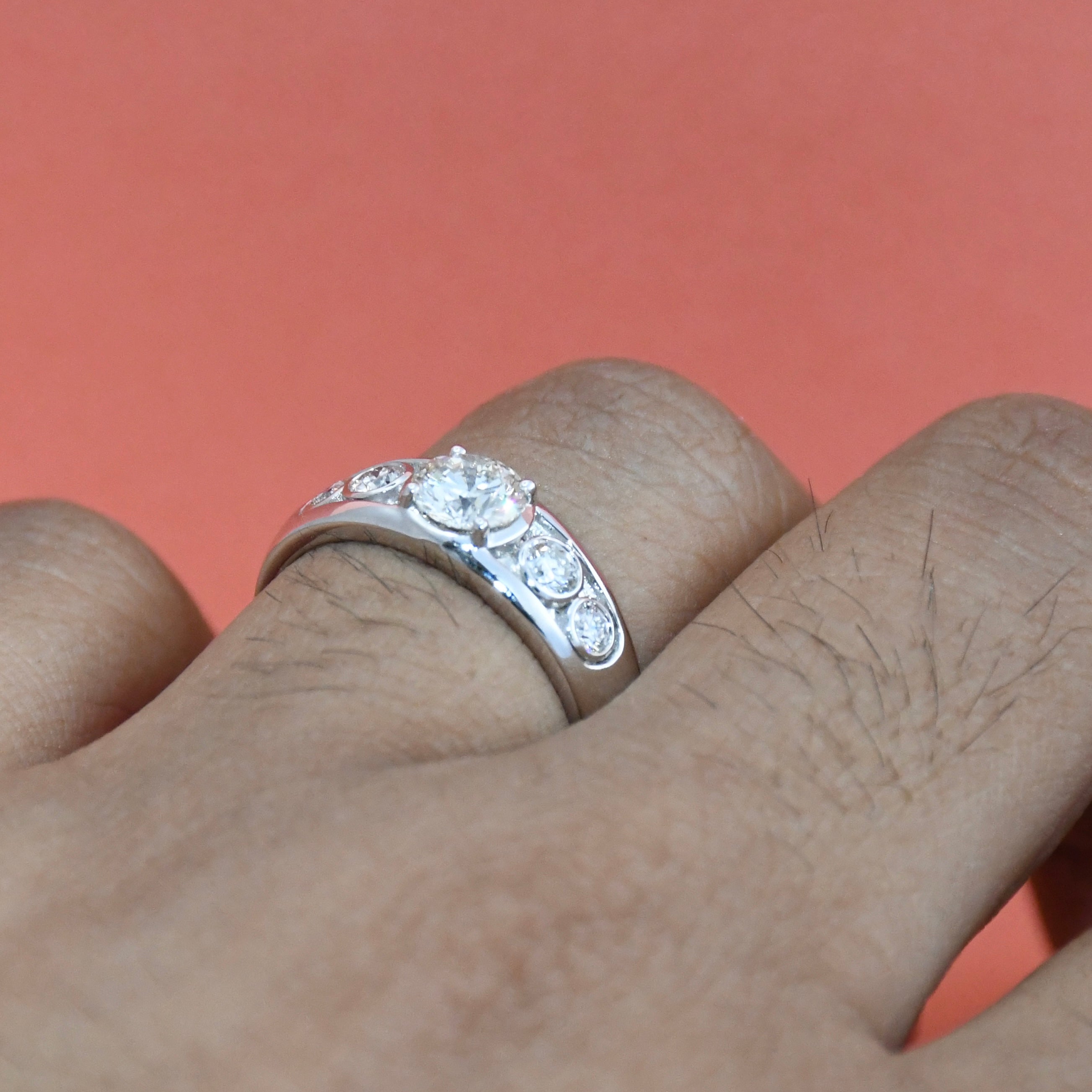 White gold ring with lab diamonds on a finger against a pink background