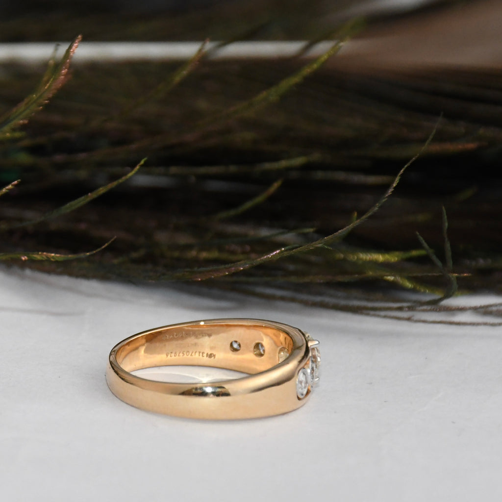 Gold ring with lab diamonds on a white surface with greenery in the background