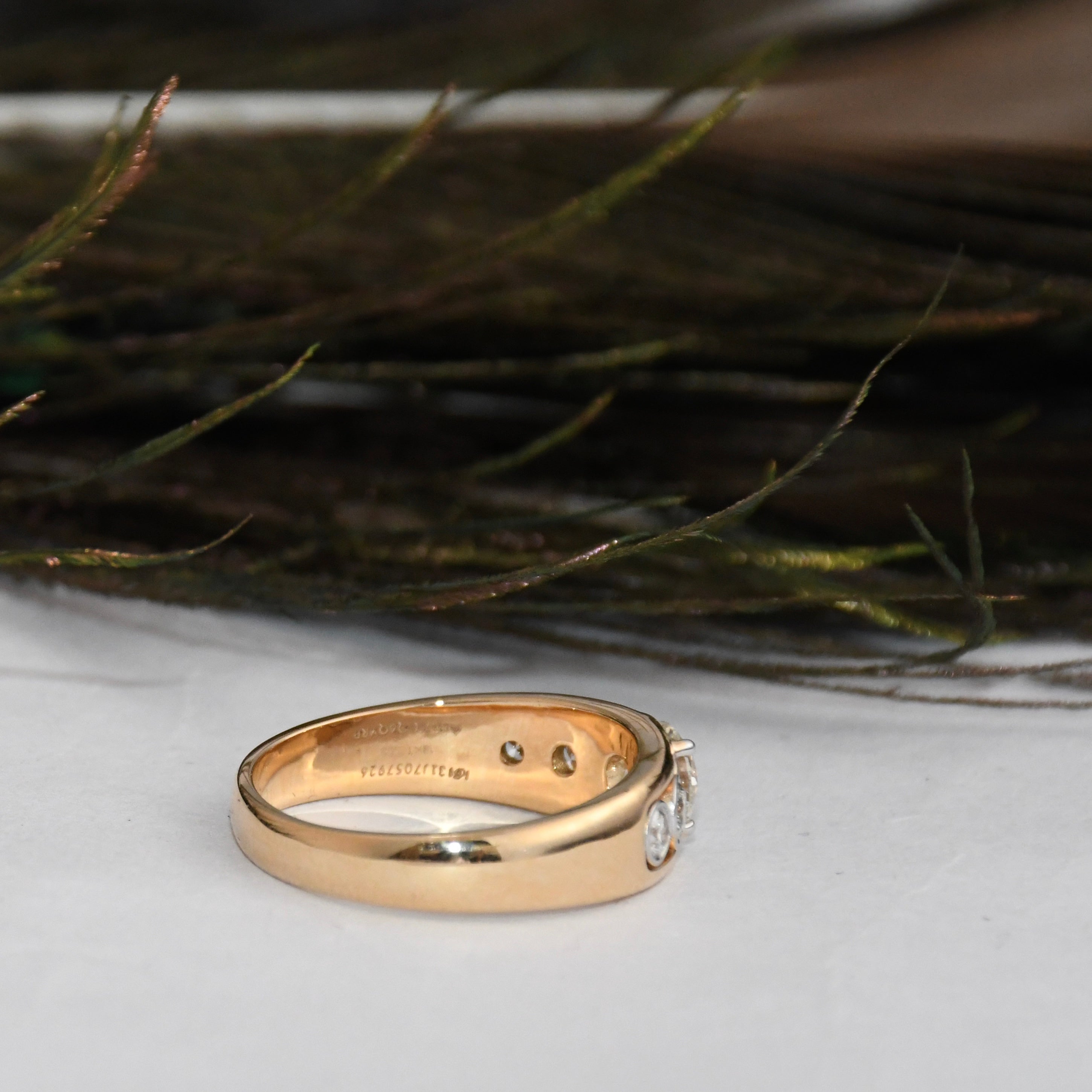 Gold ring with lab diamonds on a white surface with greenery in the background