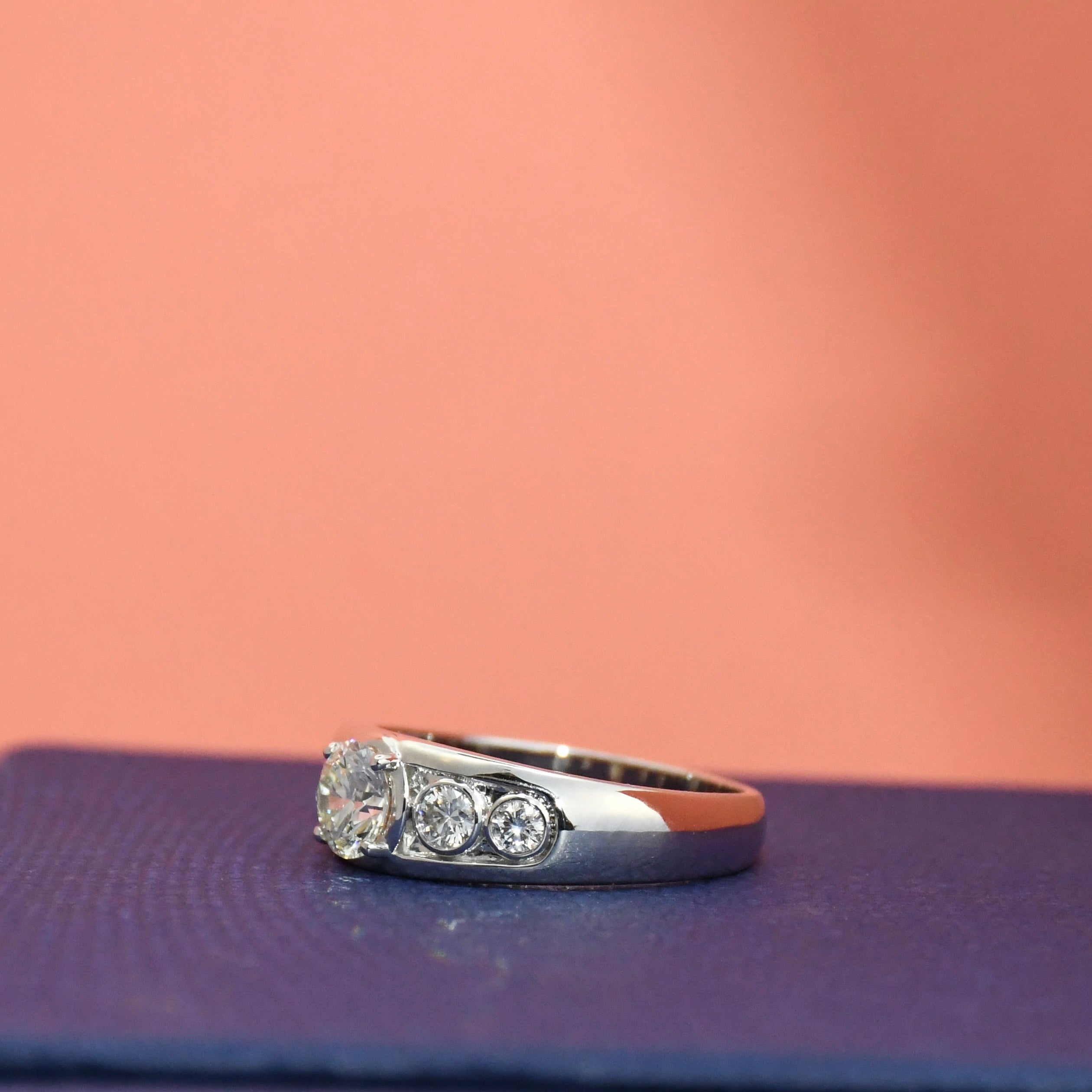 White gold ring with lab diamonds on a textured surface with a pinkish-brown background