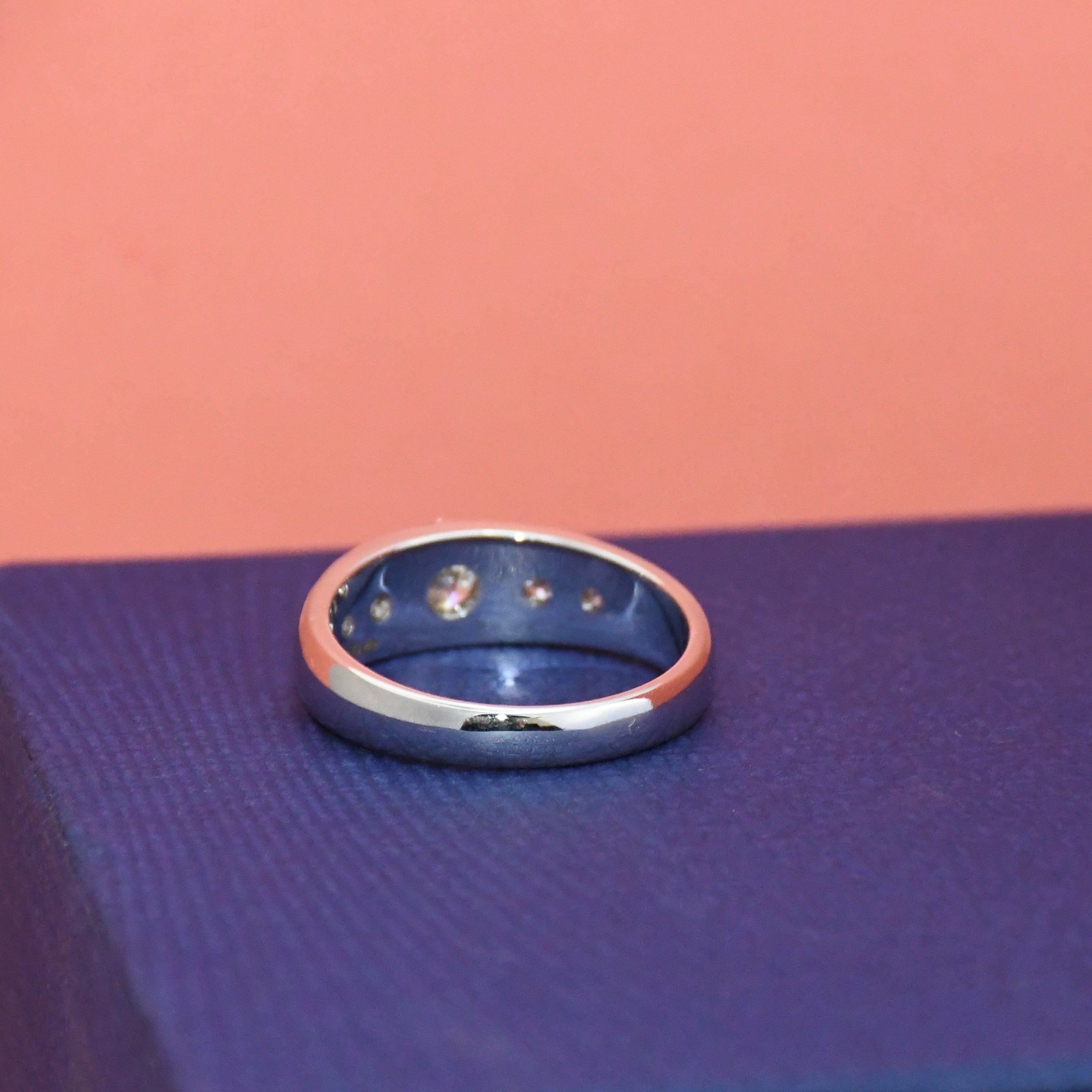 White gold ring on a textured blue surface with a pink background
