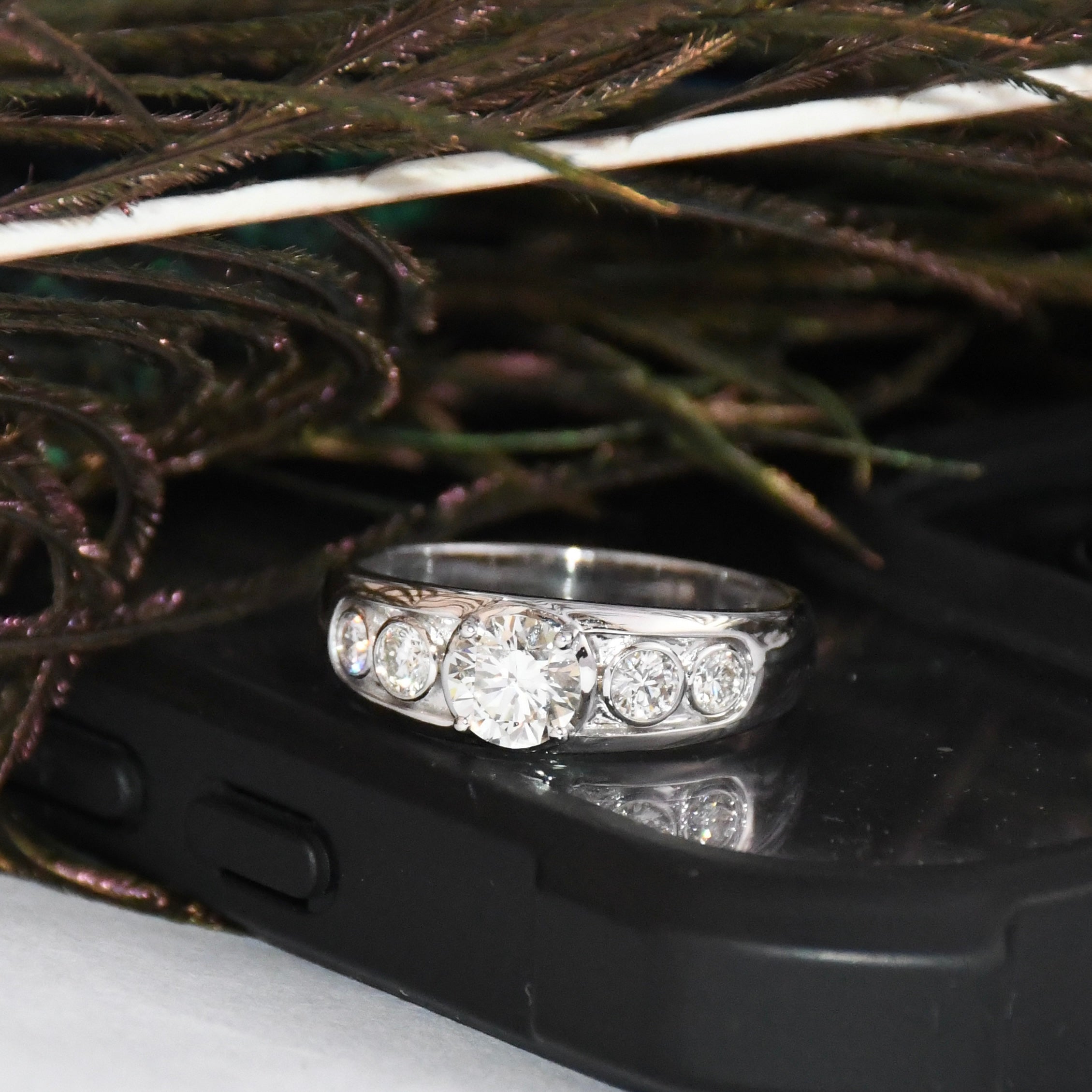 White gold ring with lab diamonds on a black phone case with feathers in the background