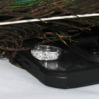 White gold ring with lab diamonds on a black phone case next to peacock feathers
