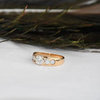 Gold ring with lab diamonds on a white surface with greenery in the background