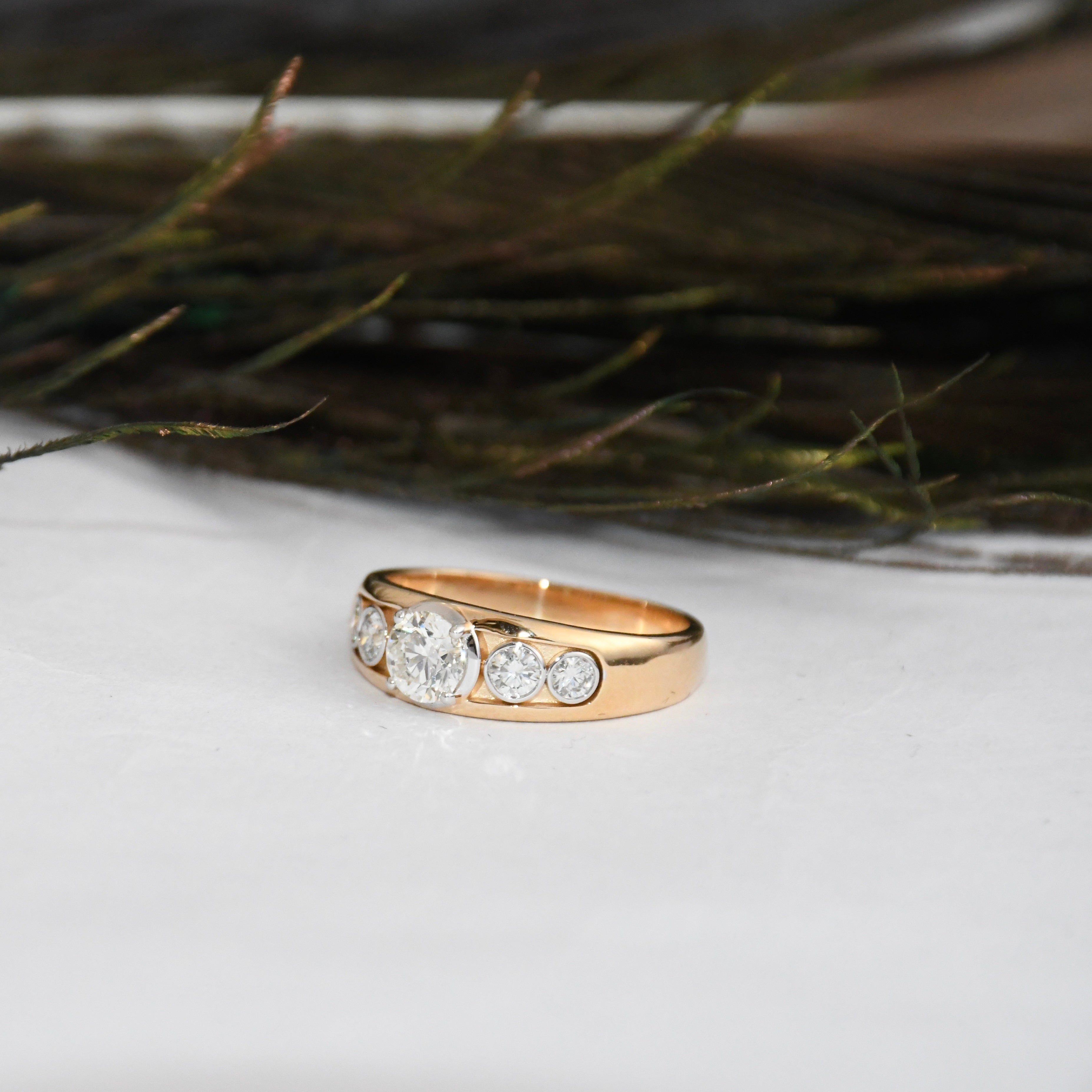 Gold ring with lab diamonds on a white surface with greenery in the background