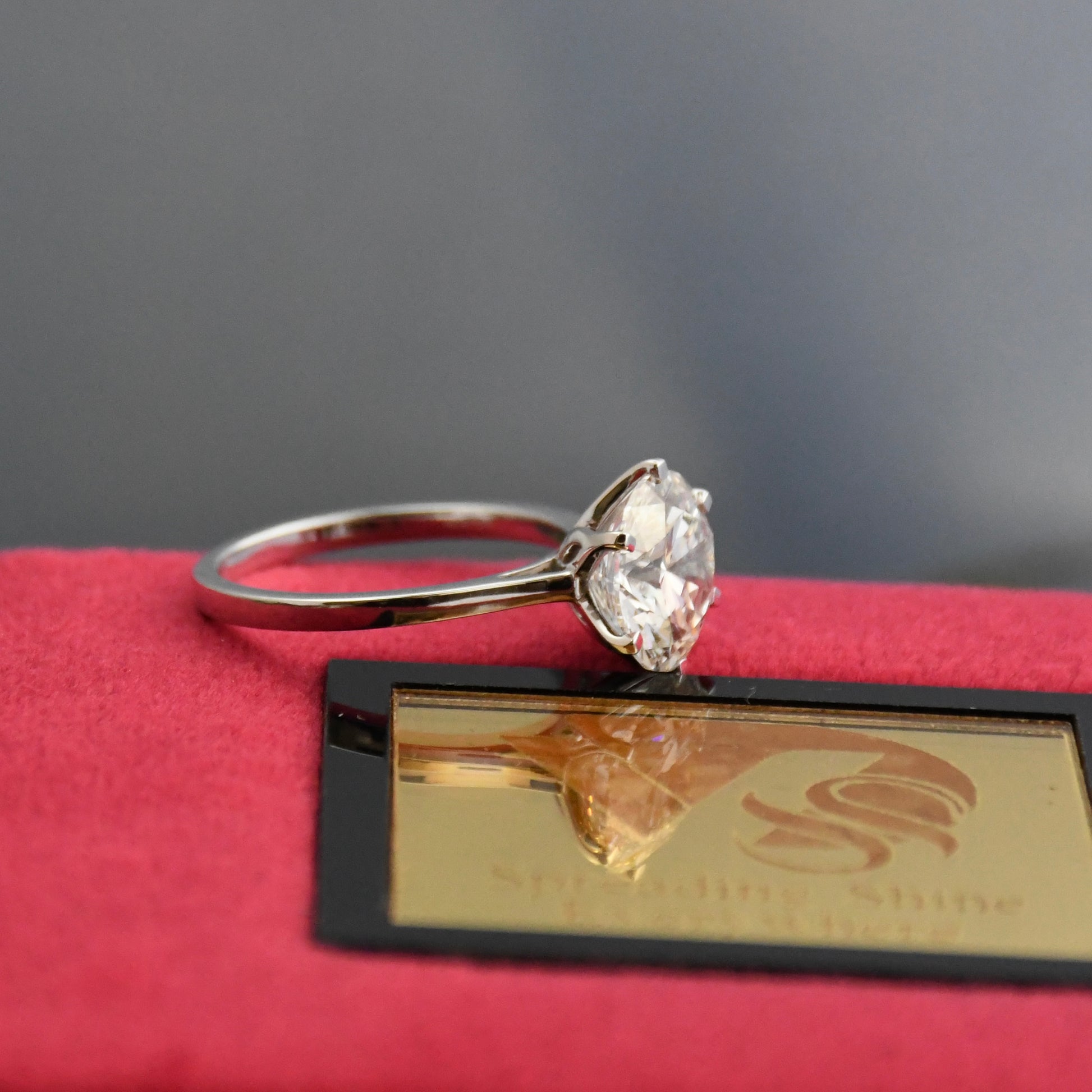 Solitaire diamond ring on a red cushion with a brand label in the background