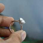 Solitaire lab grown diamond ring held between fingers against a blurred background