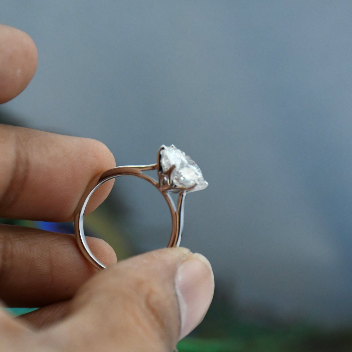 Solitaire lab grown diamond ring held between fingers against a blurred background