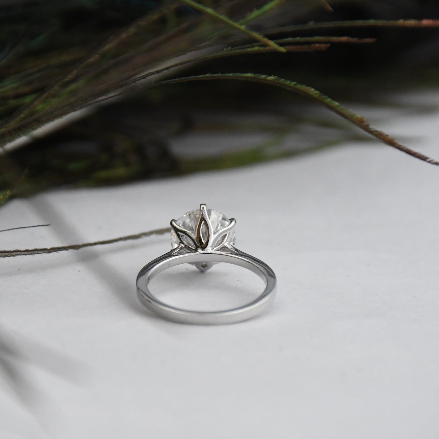 White gold ring with a solitaire lab grown diamond on a light surface with greenery in the background