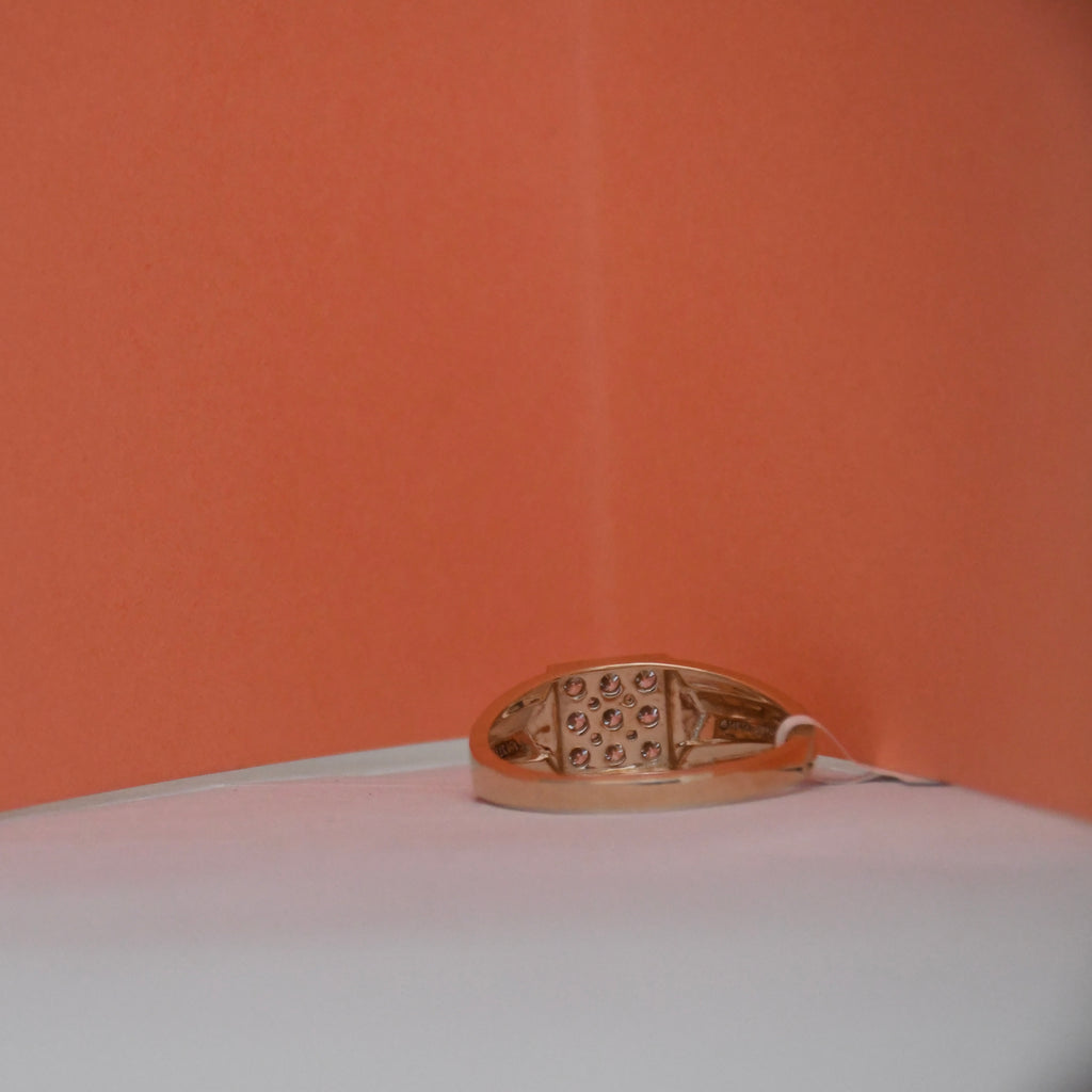 A gold ring with an intricate openwork filigree pattern on the band, resting on a white surface against a solid orange background.