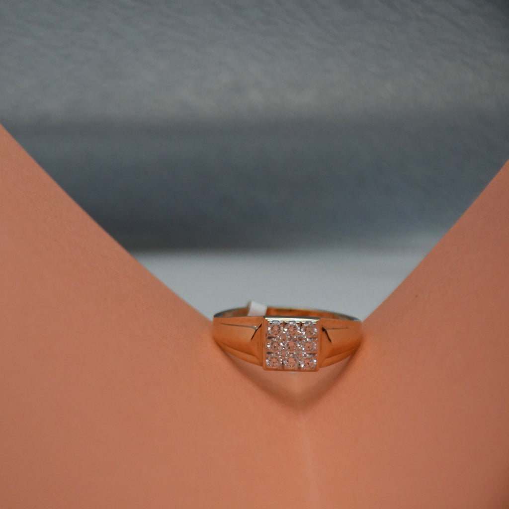A rose gold ring with a square pavé diamond setting, displayed on a peach-colored ring stand against a gray textured background.