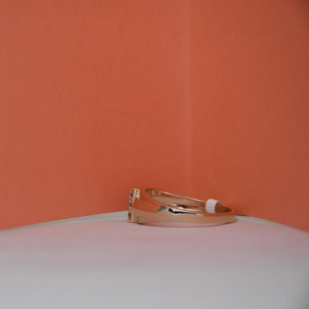 A rose gold ring with a small clear gemstone on the band, resting on a white surface against a textured orange background.