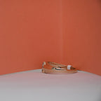 A rose gold ring with a small clear gemstone on the band, resting on a white surface against a textured orange background.