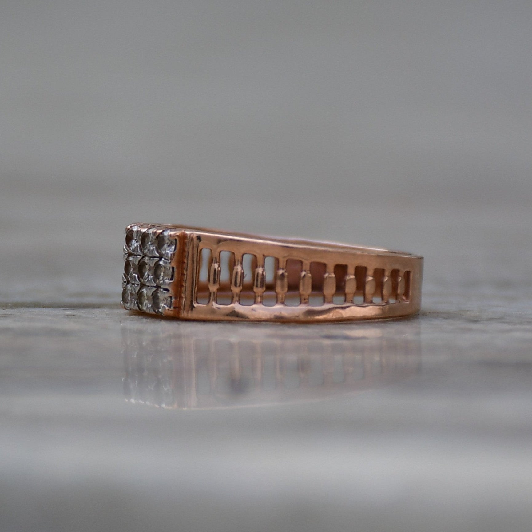 A gold diamond ring is displayed on a grey surface.