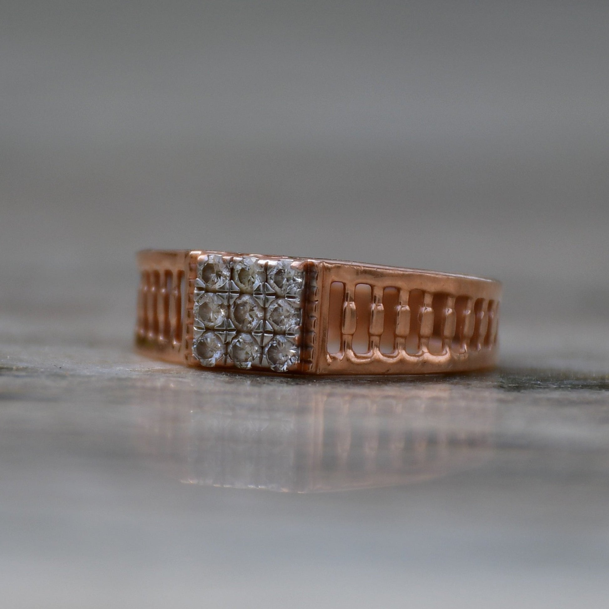 A gold diamond ring is displayed on a grey surface.