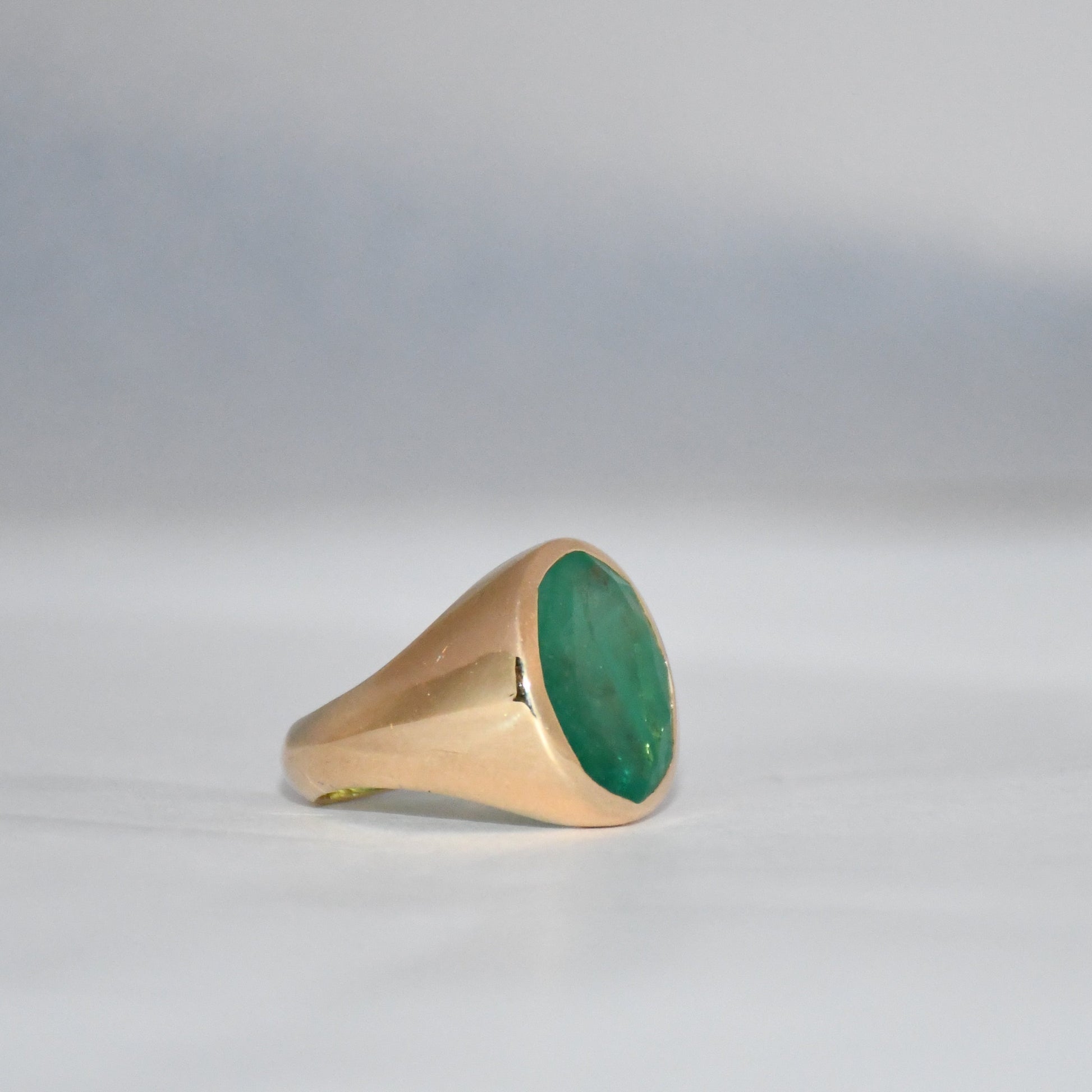 Gold ring with a green emerald stone on a gray background