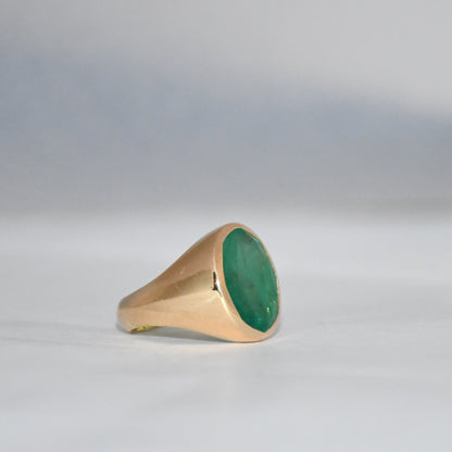 Gold ring with a green emerald stone on a gray background