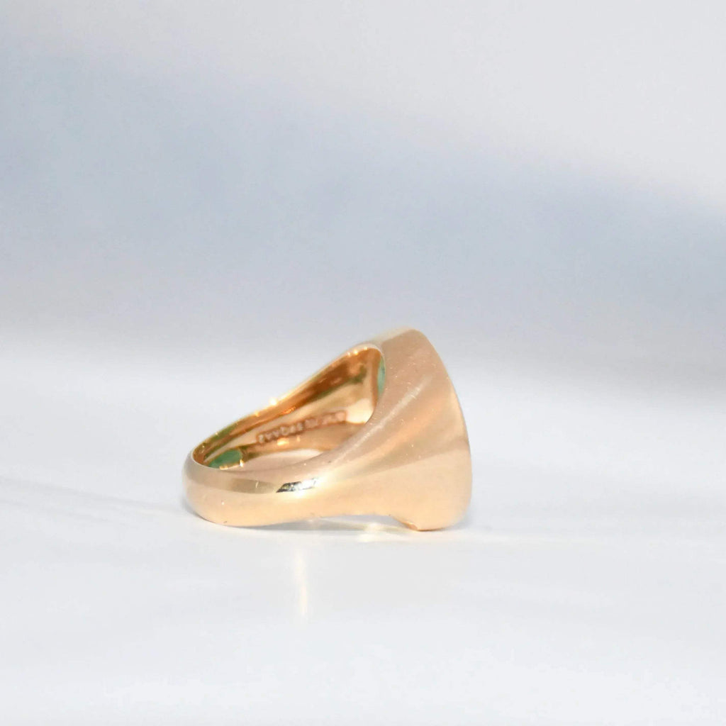 Gold ring with a green emerald stone on a gray background.