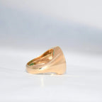 Gold ring with a green emerald stone on a gray background.