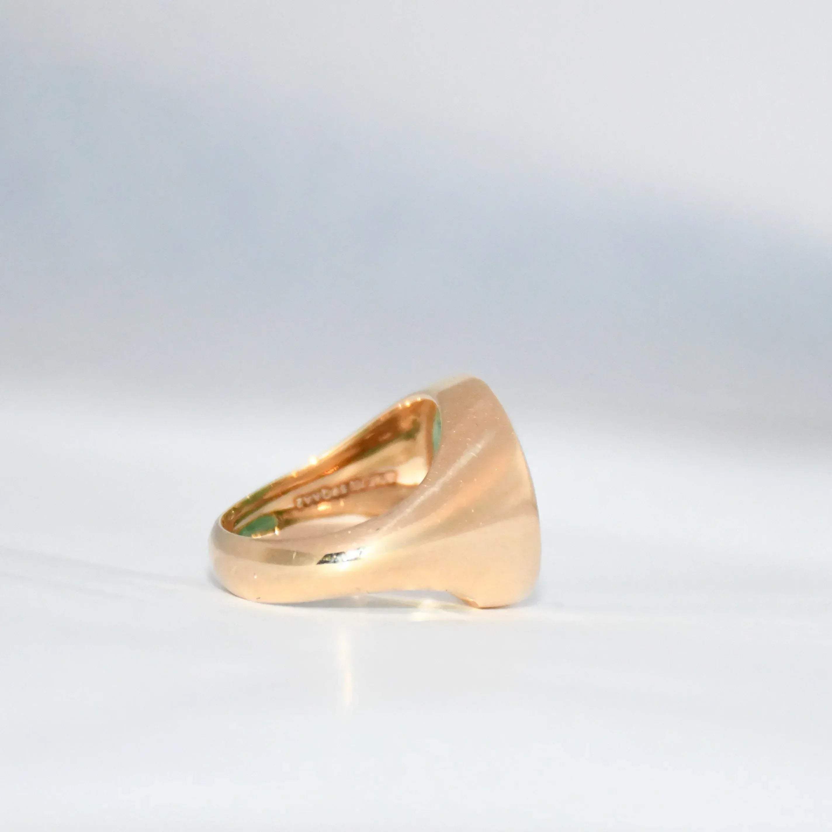 Gold ring with a green emerald stone on a gray background.