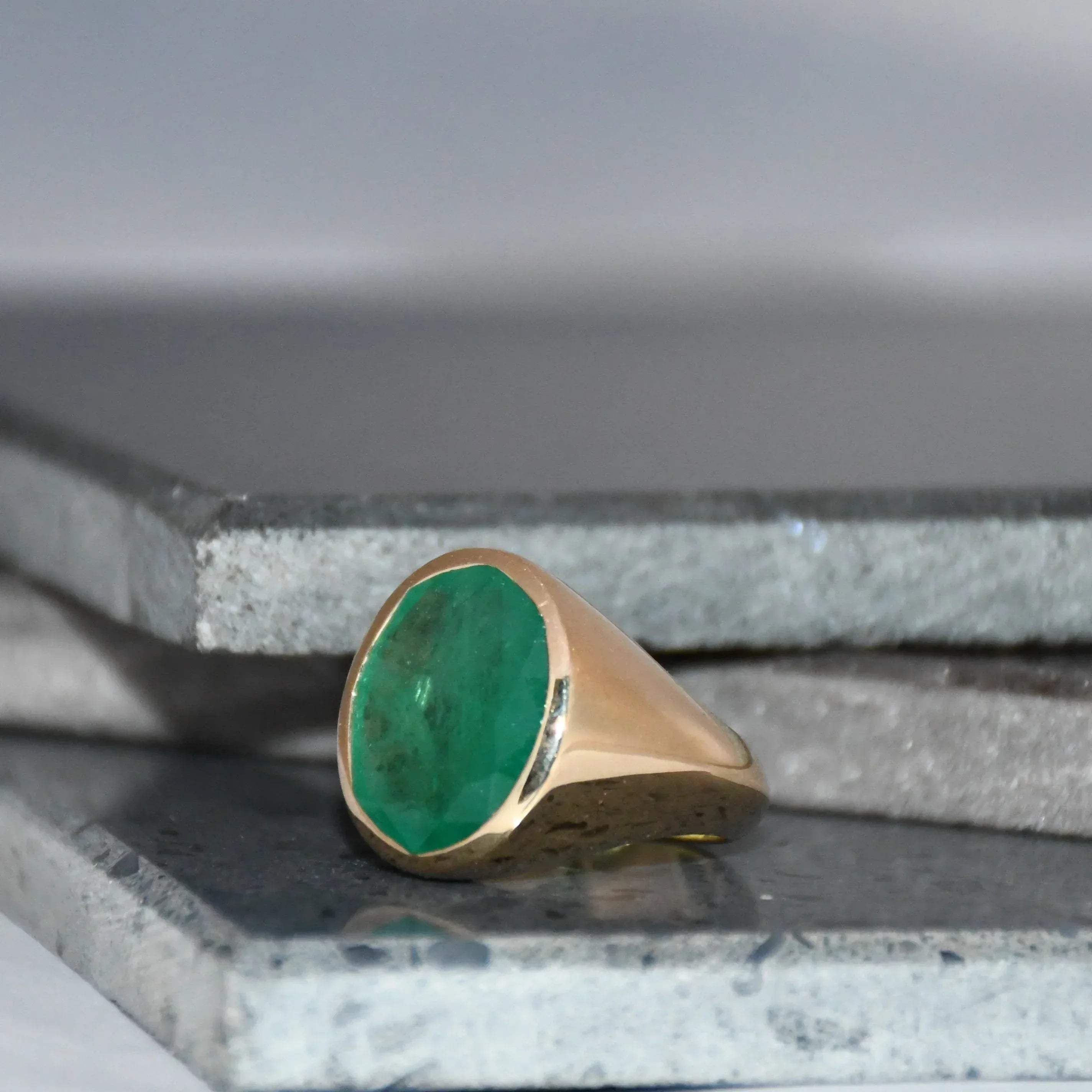 Gold ring with a green emerald gemstone on a gray surface