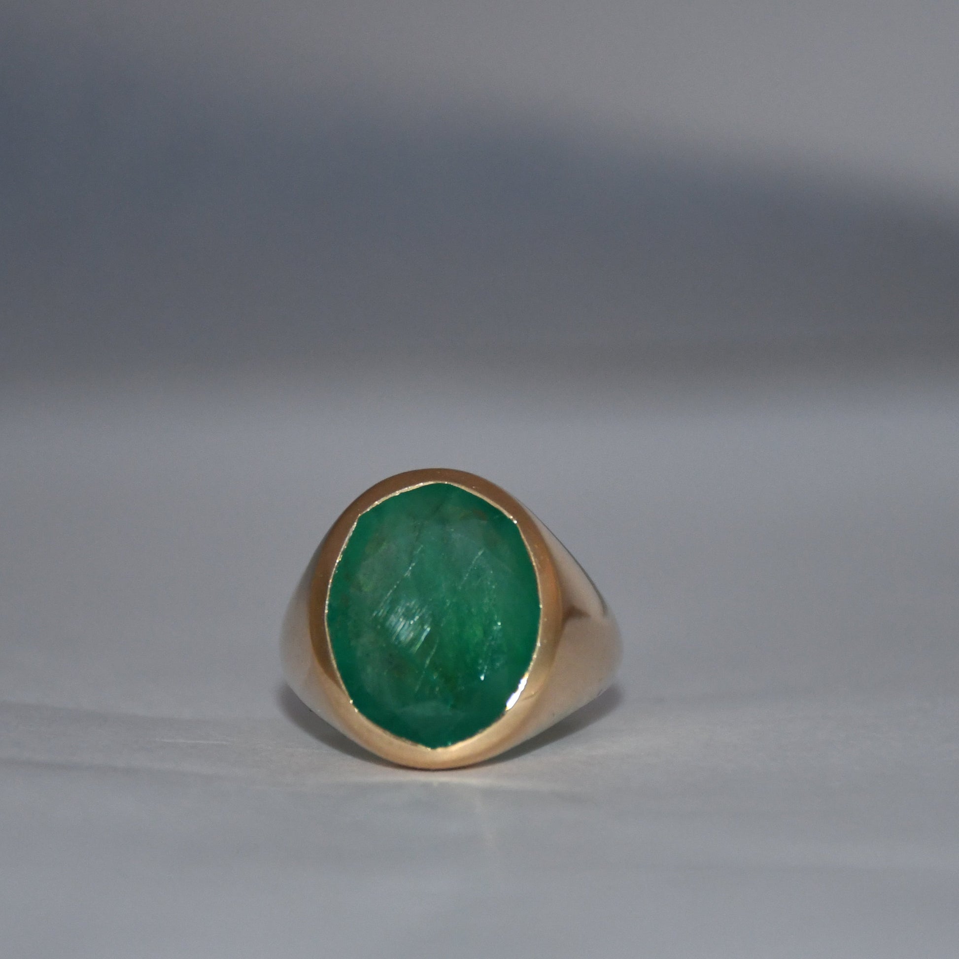 Gold ring with a green emerald gemstone on a gray background