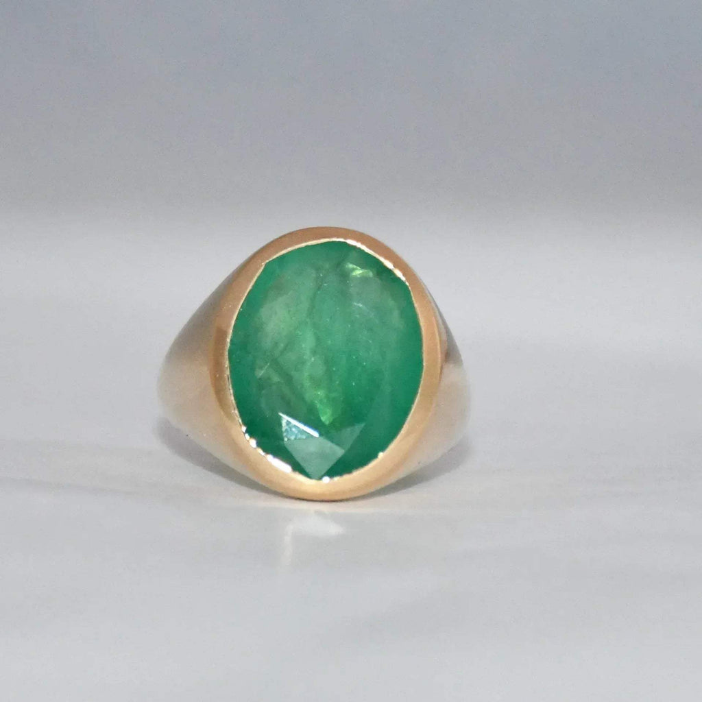Gold ring with a green emerald stone on a gray background