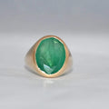 Gold ring with a green emerald stone on a gray background
