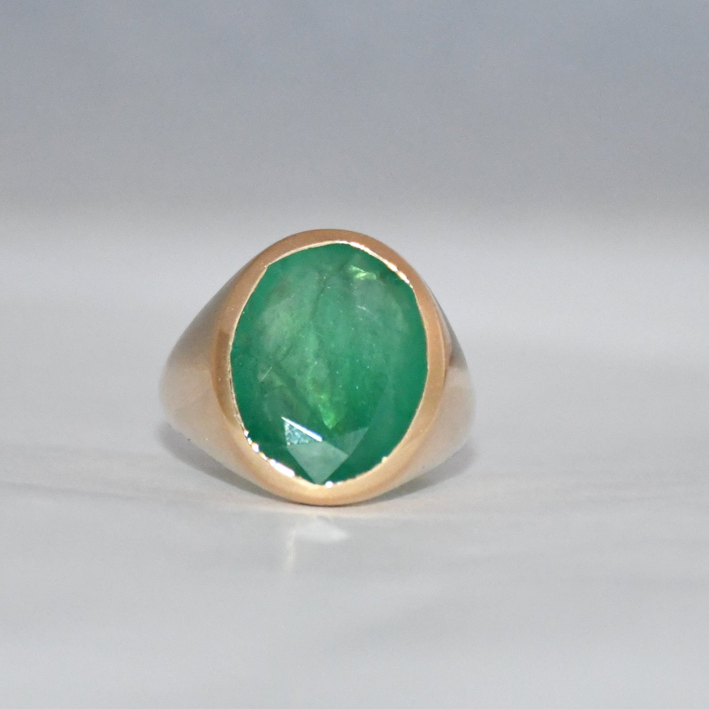 Gold ring with a green emerald stone on a gray background