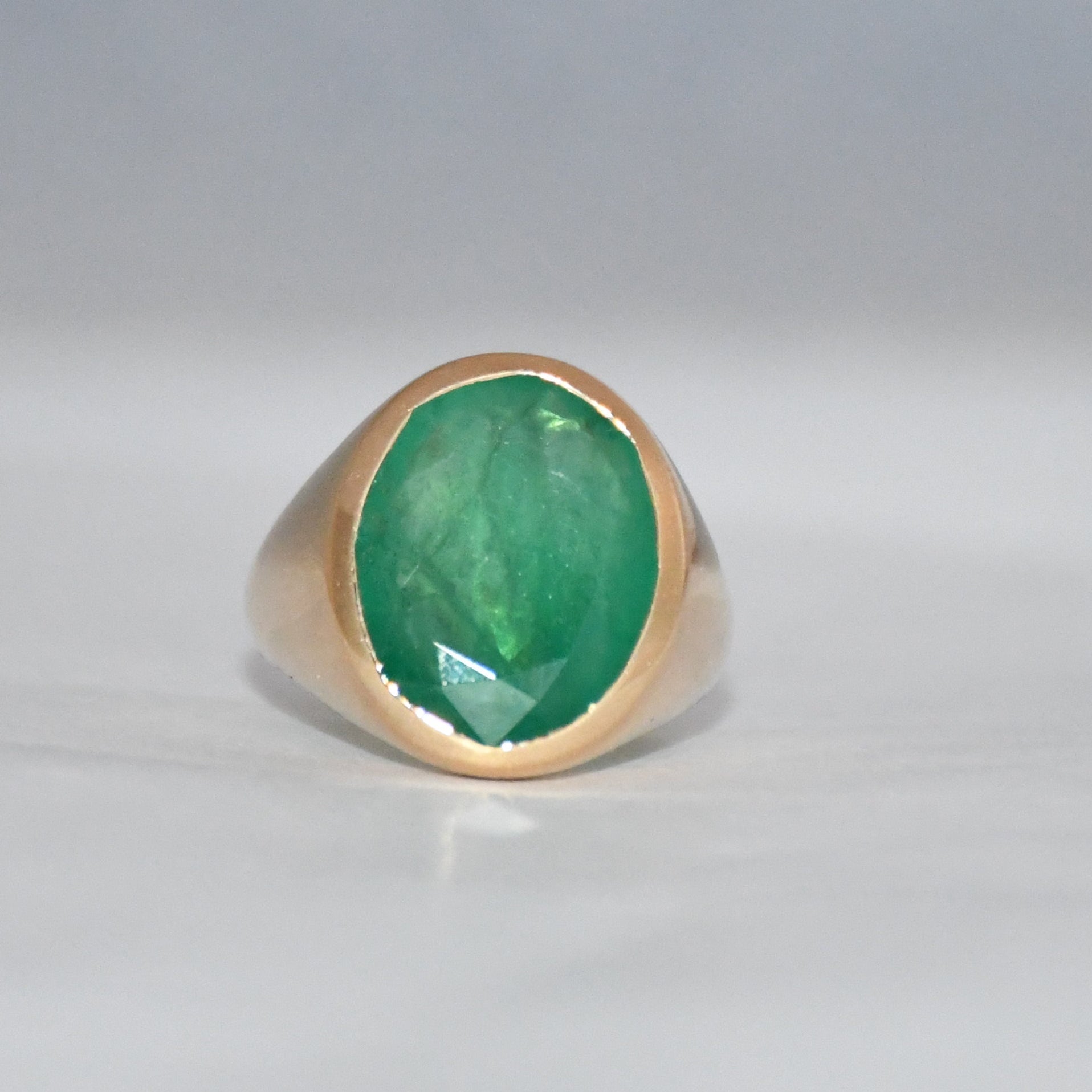 Gold ring with a green emerald stone on a gray background