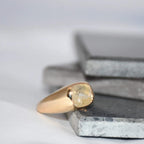 Gold ring with a natural sapphire gemstone on a textured surface with a neutral background