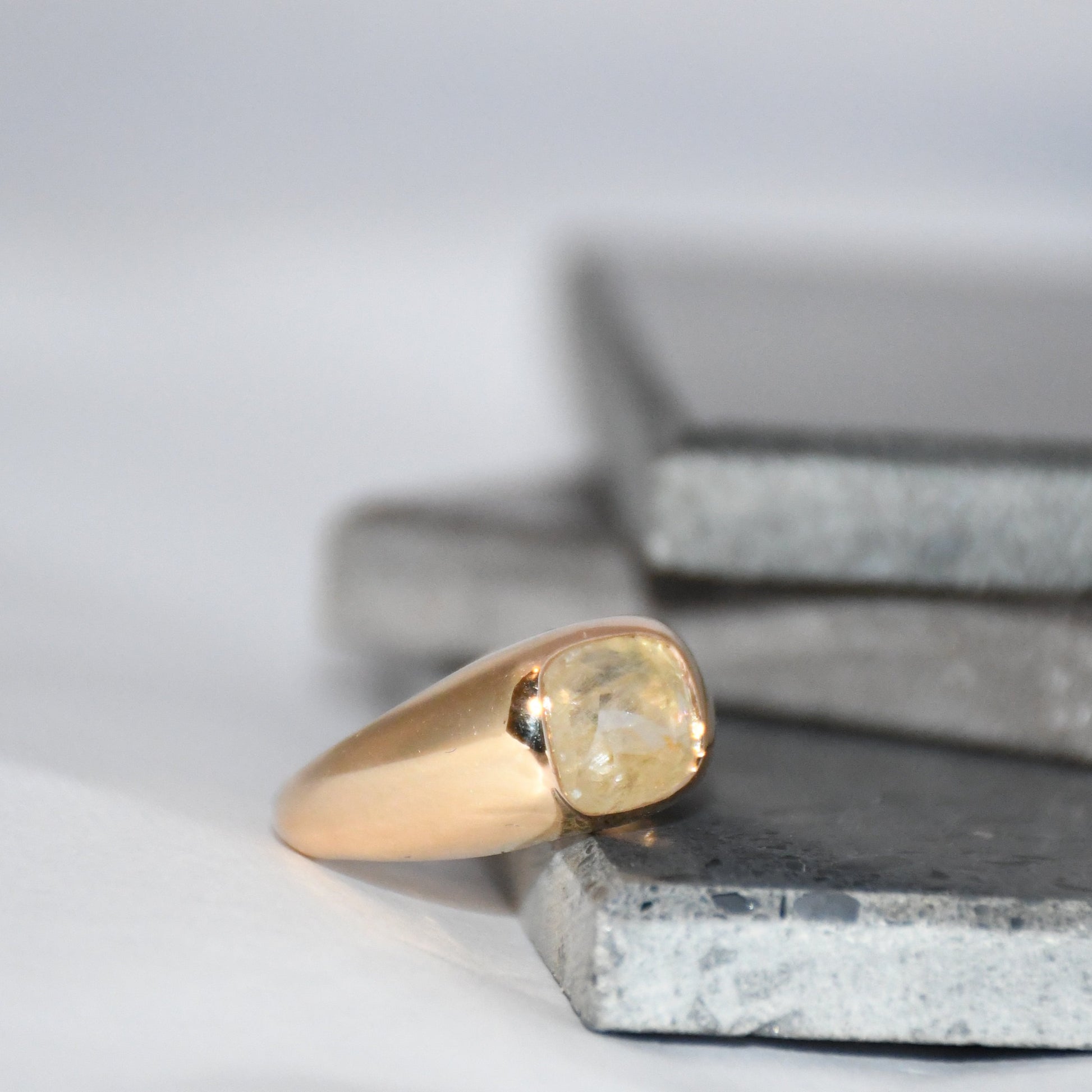 Gold ring with a natural sapphire gemstone on a textured surface with a neutral background