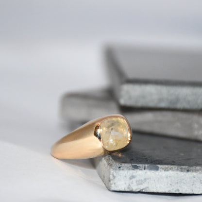 Gold ring with a natural sapphire gemstone on a textured surface with a neutral background