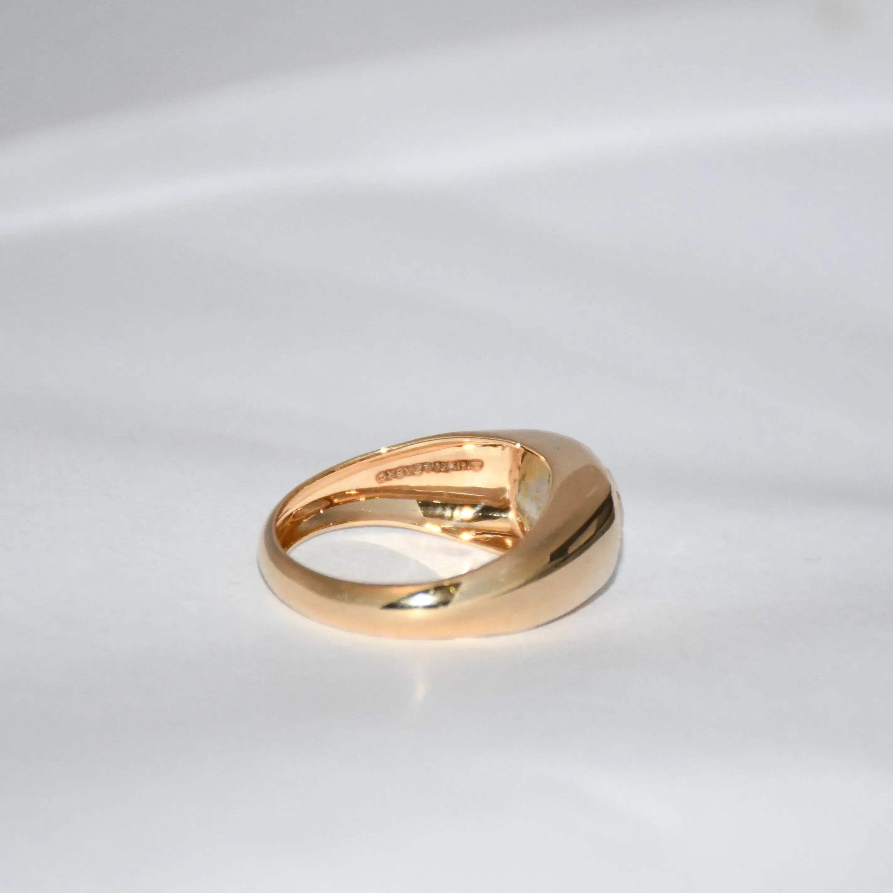 A gold ring with natural sapphire gemstone is displayed on a white surface.