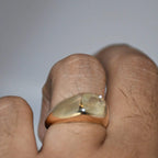 Gold ring with a natural yellow sapphire on a finger against a plain background