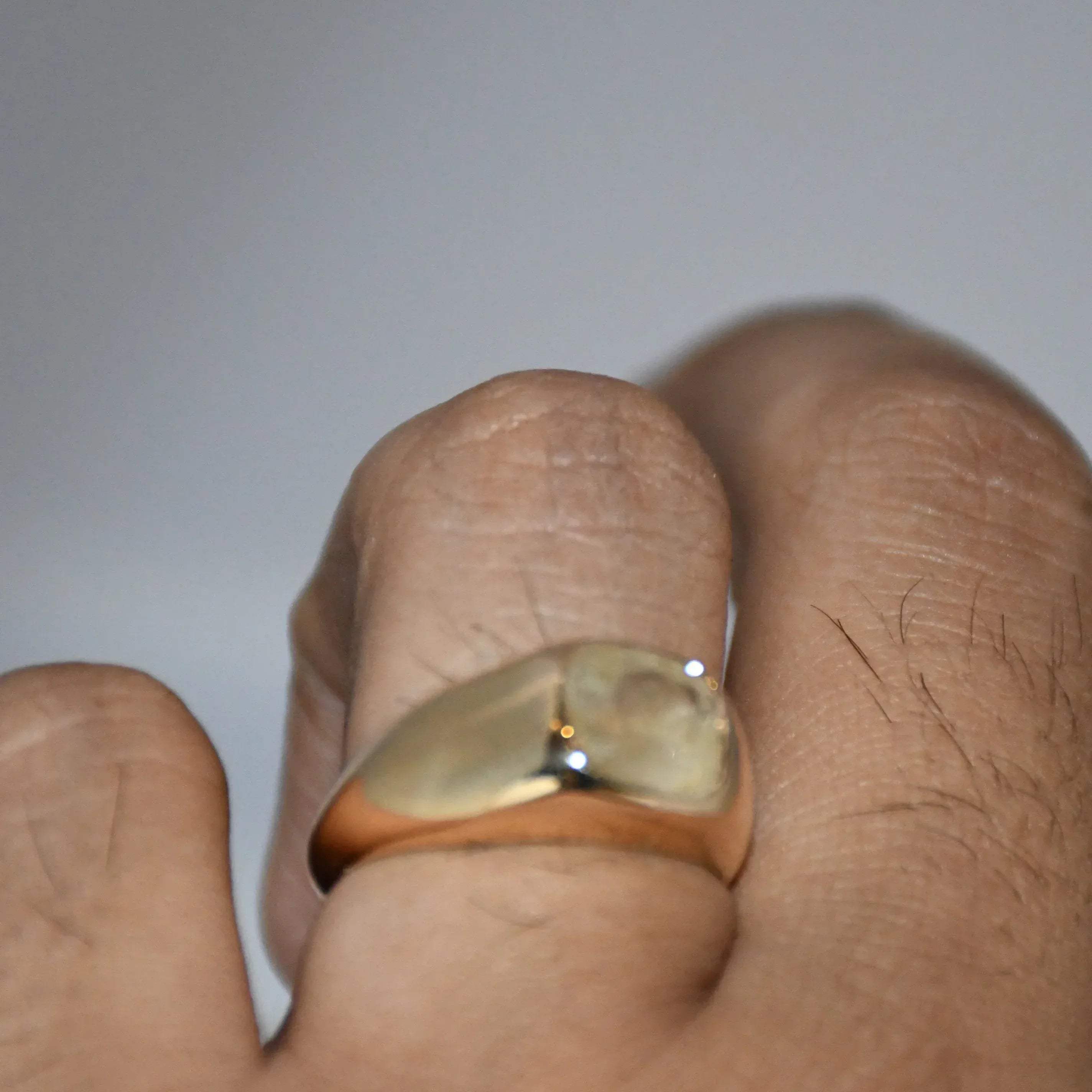Gold ring with a natural yellow sapphire on a finger against a plain background