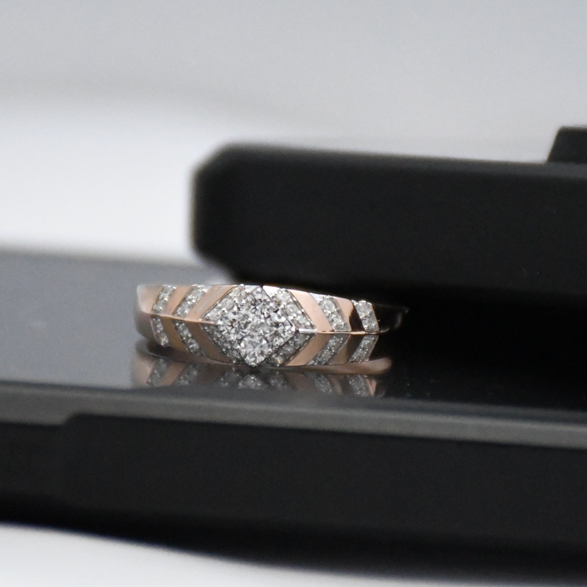 Rose gold ring with diamonds on a reflective surface