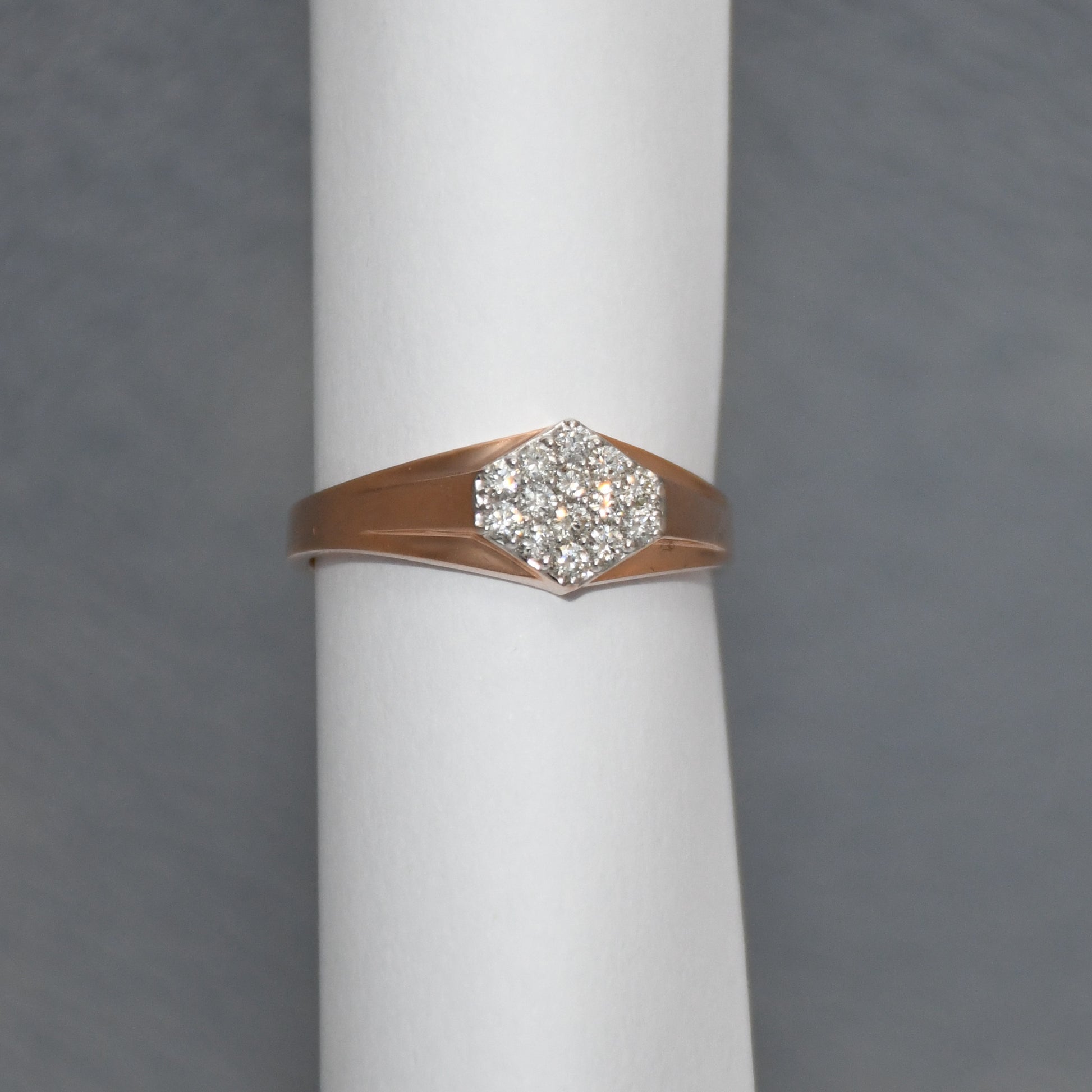 gold ring with diamond on a white cylindrical stand against a gray background